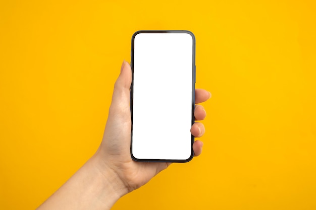 Persona que tiene un teléfono móvil con pantalla blanca en blanco sobre un fondo amarillo, espacio de copia