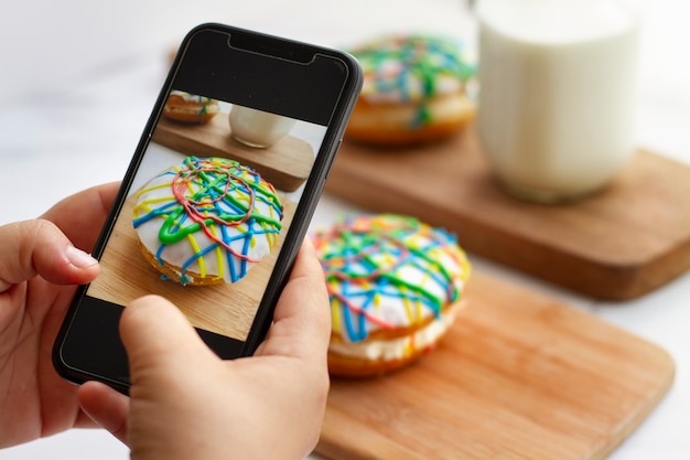 Foto persona que toma una foto de donas con cobertura colorida con teléfono inteligente