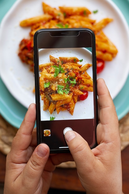 Persona que toma una foto de un plato de pasta con un teléfono inteligente