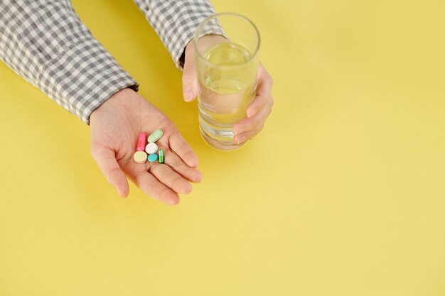 Persona que toma un puñado de pastillas y tabletas y un vaso de agua