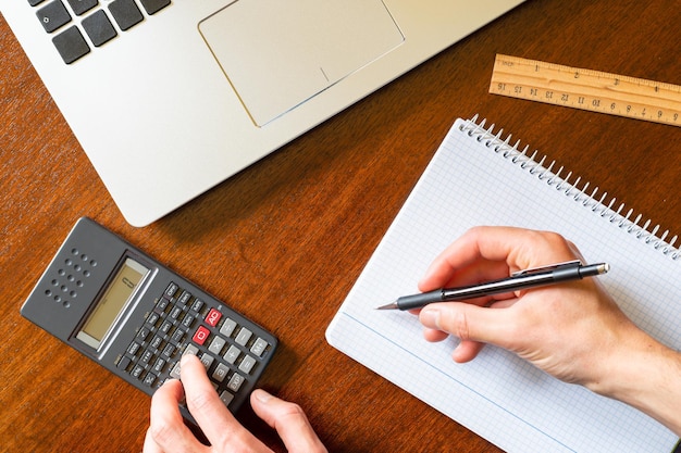 Persona que trabaja con calculadora, cuaderno y bolígrafo Espacio de trabajo Solo se pueden ver las manos