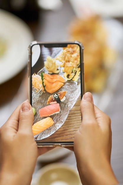 Foto persona que usa una cámara móvil para fotografiar comida de sushi