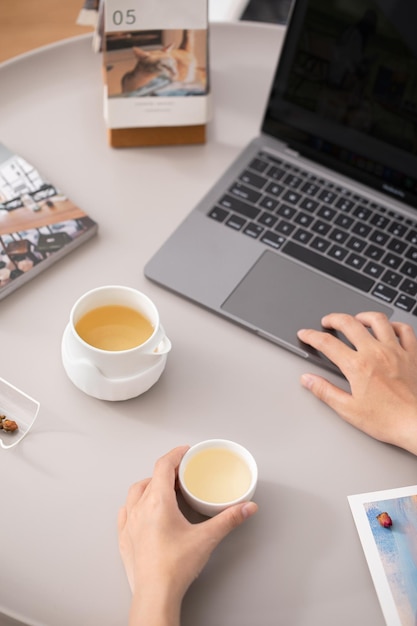 Una persona que usa una computadora portátil con una taza de té en la mesa Perfiles de sabor de té según la técnica de preparación