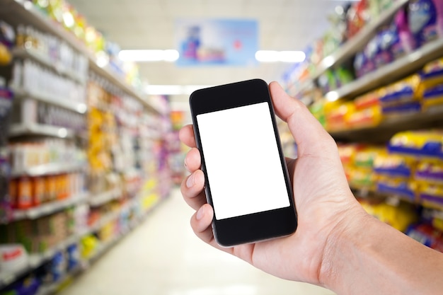 Persona que usa el sostenedor blanco de la pantalla del smartphone en la mano con los estantes en fondo en supermercado.