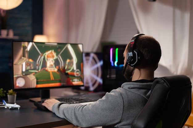 Persona que usa el teclado y el mouse para jugar videojuegos en la computadora. Hombre usando auriculares y jugando juegos en línea con mousepad y equipo de juego. Jugador haciendo actividad para entretenimiento.