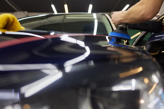 Persona que utiliza una máquina para pulir el exterior de automóviles negros