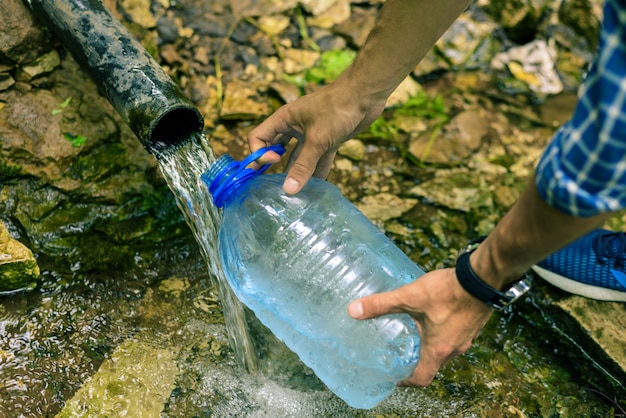 Una persona recoge agua limpia de un manantial en una botella de plástico.