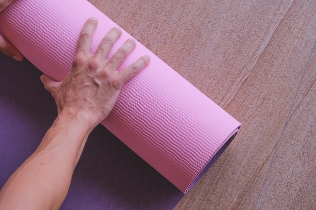 Una persona rodando una colchoneta de yoga rosa en el suelo