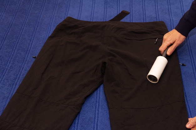 Persona con rodillo adhesivo para limpiar ropa, limpiar pantalones negros