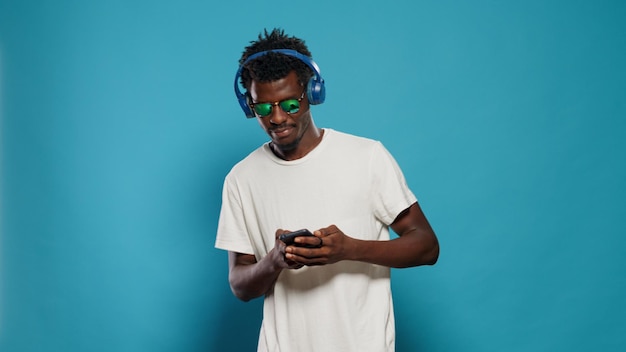 Persona saltando y escuchando música mientras usa un teléfono inteligente. Joven bailando y disfrutando de la canción en los auriculares para entretenerse. Adulto moderno con gafas de sol y auriculares para divertirse