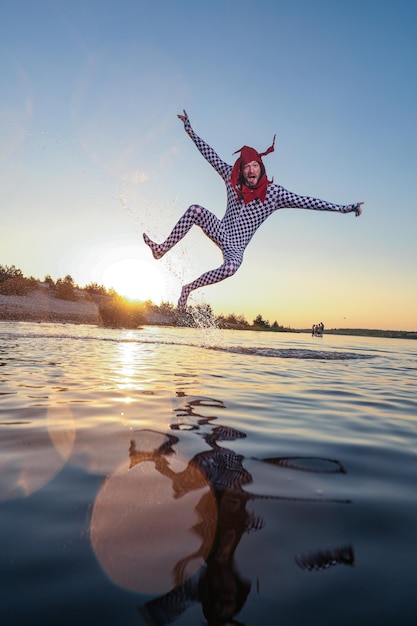 Foto persona saltando en el mar contra el cielo durante la puesta del sol