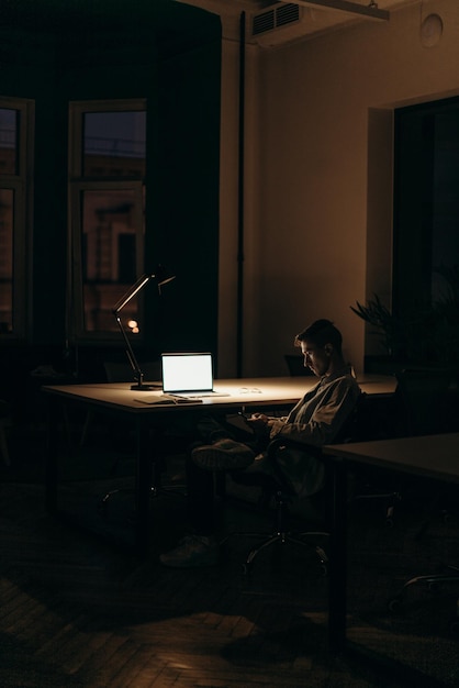 Una persona sentada en un escritorio con una computadora portátil y una lámpara.