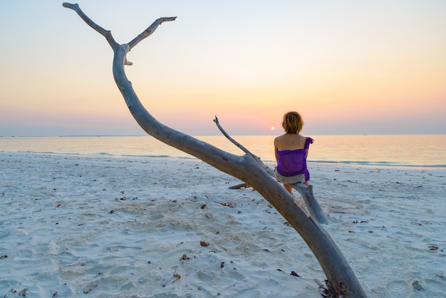 Una persona sentada en la rama en la playa al atardecer