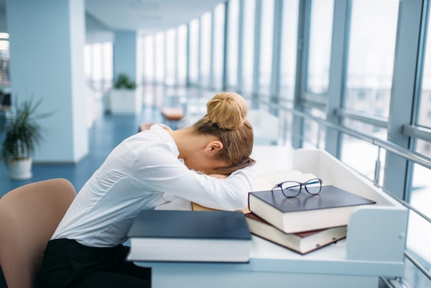 Persona del sexo femenino durmiendo en la mesa en la biblioteca