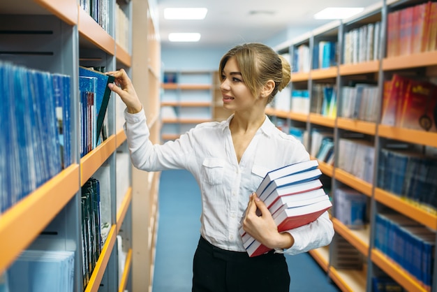 Persona de sexo femenino con pila de libros en la biblioteca