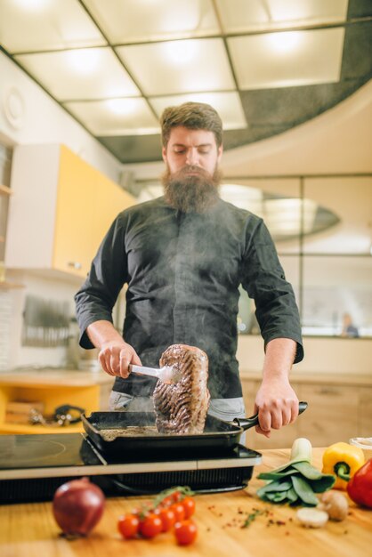 Persona del sexo masculino cocinar carne en una sartén en la cocina