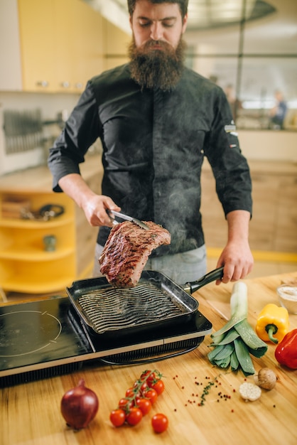 Persona del sexo masculino cocinar carne en una sartén en la cocina