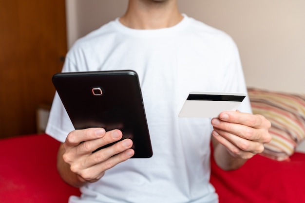 Foto persona del sexo masculino haciendo compras online con su tableta y pagando con tarjeta de crédito