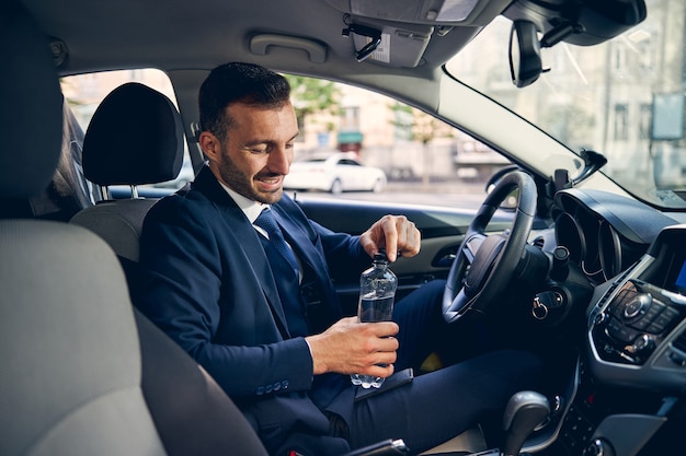 Persona de sexo masculino morena encantada positiva abriendo la botella con agua mientras va a refrescarse en un día caluroso