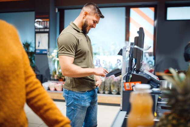 Persona de sexo masculino paga en la caja en la tienda de comestibles