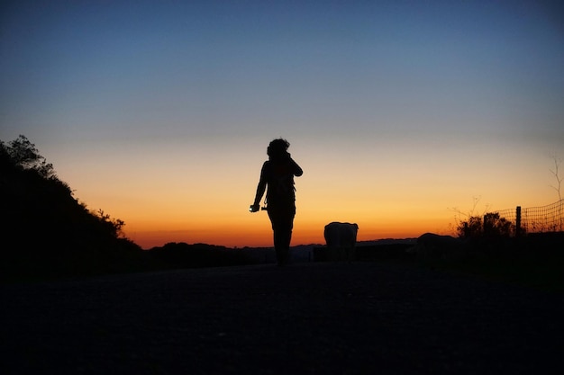 Persona en silueta caminando por el campo contra el cielo durante la puesta de sol