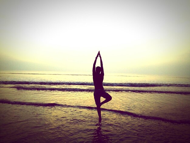 Persona de silueta haciendo yoga en la playa