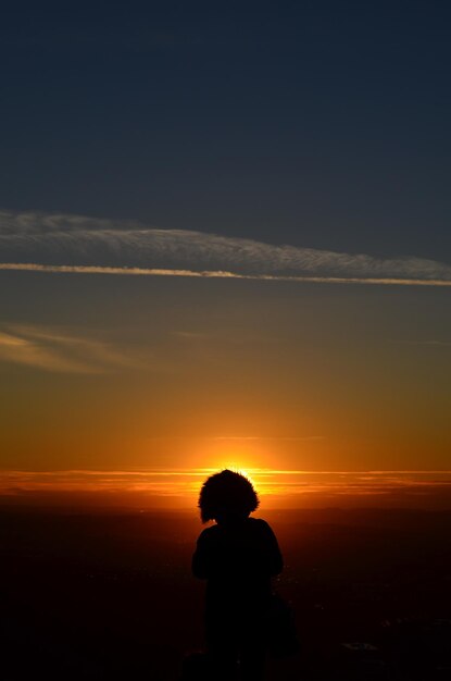Persona en silueta de pie contra el cielo naranja durante la puesta de sol