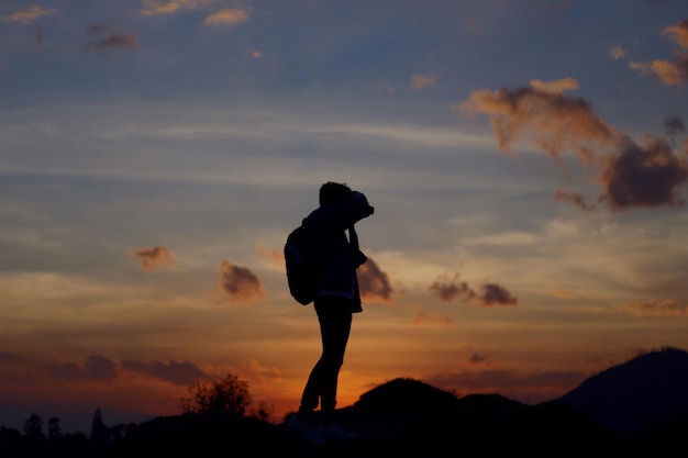Foto persona en silueta de pie en la montaña contra el cielo durante la puesta de sol