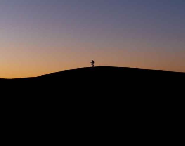 Foto persona en silueta de pie en la orilla contra el cielo durante la puesta de sol