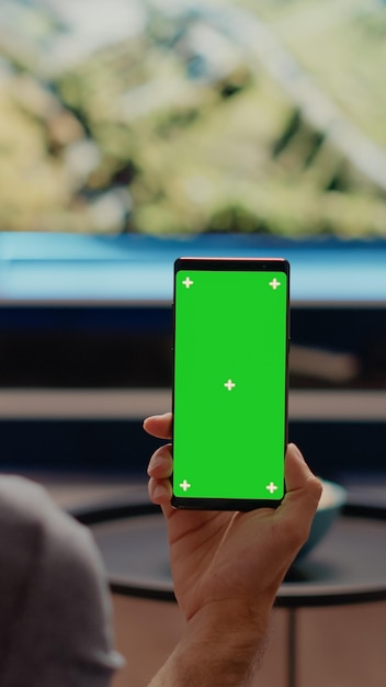 Persona con smartphone moderno mirando fondo vertical de pantalla verde en la sala de estar. Hombre caucásico con clave de croma y pantalla de medios aislados para plantilla de espacio de copia de maqueta