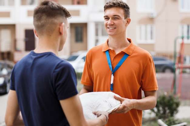 Una persona sonriente que lleva una camiseta naranja y una etiqueta con su nombre entrega un paquete a un cliente. Trabajador amable, servicio de entrega de alta calidad.