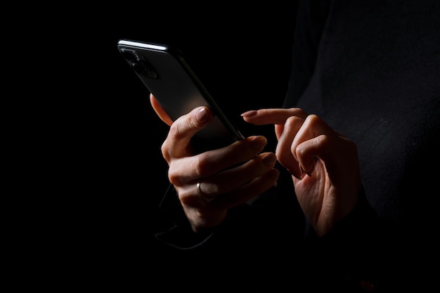 Persona sosteniendo en las manos y escribiendo en la foto del teléfono móvil aislado sobre fondo negro