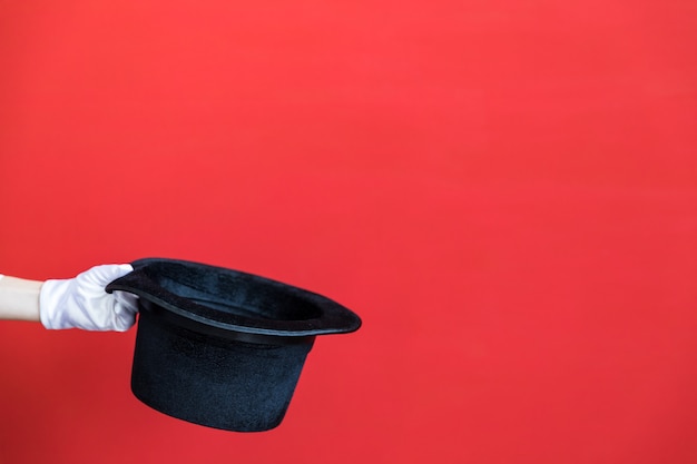 Foto persona sosteniendo sombrero de copa mágico en la mano contra la pared roja