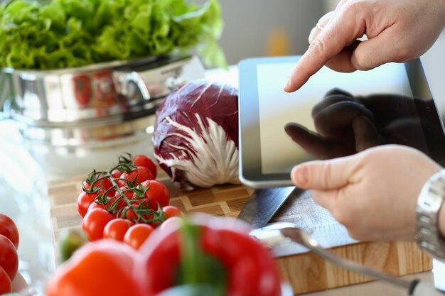 La persona sostiene la tableta y va a cocinar verduras.