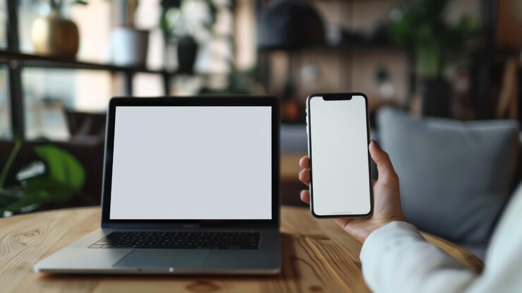 Una persona sostiene un teléfono celular frente a una computadora portátil
