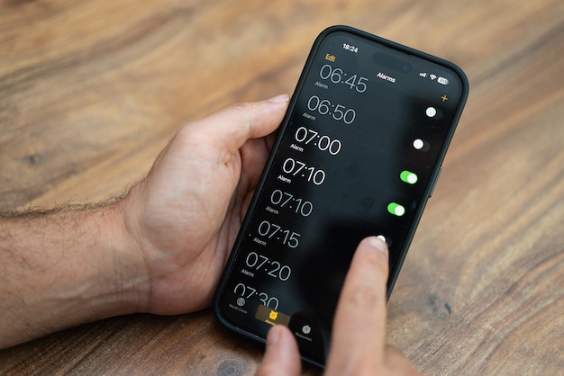 La persona sostiene el teléfono inteligente y establece la hora en la aplicación del despertador para asegurarse de recibir notificaciones para despertarse