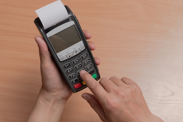 Una persona tiene en su mano una terminal para pagar las compras en una tienda usando tarjetas bancarias o NFC