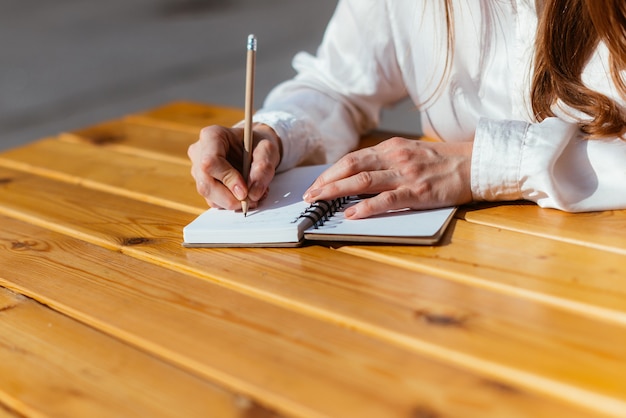 Persona toma notas con un lápiz en un cuaderno mientras está sentado en un café en el verano en la calle