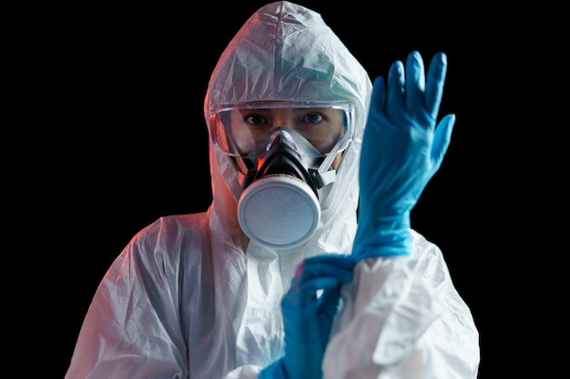 Persona en traje de protección con guantes de goma en la pared oscura