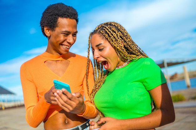 Persona transgénero y mujer afro compartiendo teléfono móvil y riendo