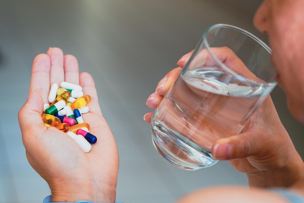 Una persona con varias píldoras medicinales y un vaso de agua.