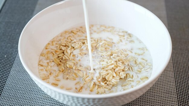 La persona vierte leche fresca en un tazón con cereales de papilla