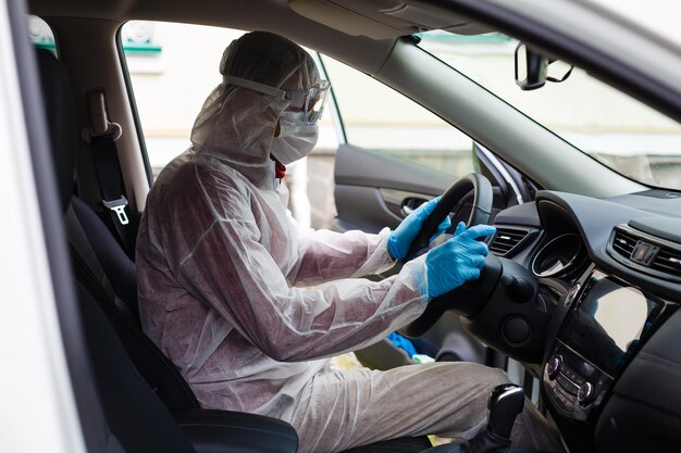 Personagem de trabalhador desinfetante em máscara protetora e terno pulveriza bactérias ou vírus em um carro.