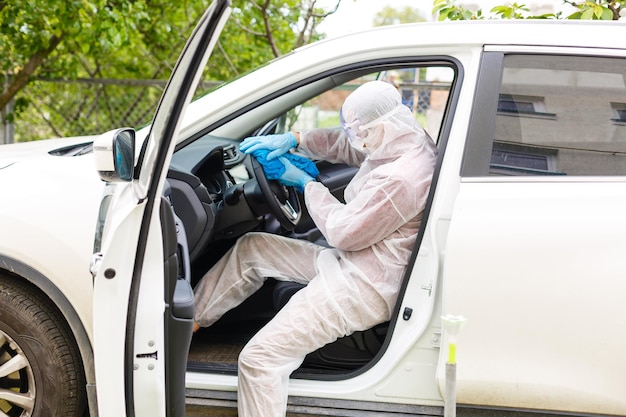 Personagem de trabalhador desinfetante em máscara protetora e terno pulveriza bactérias ou vírus em um carro.