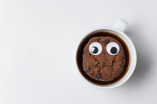 El personaje de galleta con chispas de chocolate flota en una taza de té. Taza de café con galletas en la pared blanca. Vista superior