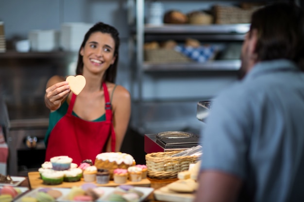 Personal femenino sonriente dando galletas con forma de corazón al cliente en el mostrador