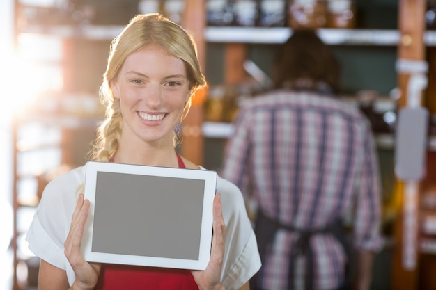 Foto personal femenino sonriente que muestra la tableta digital en supermercado