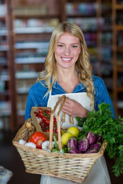 Personal femenino sonriente que sostiene la cesta de verduras en la sección orgánica