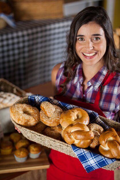 Personal femenino sonriente sosteniendo una cesta de mimbre de varios panes en el mostrador