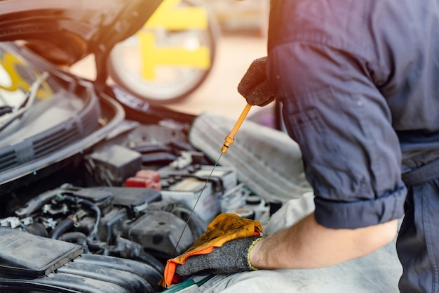 Personal mecánico que busca revisión y cambio de aceite de motor de automóvil con varilla en el garaje